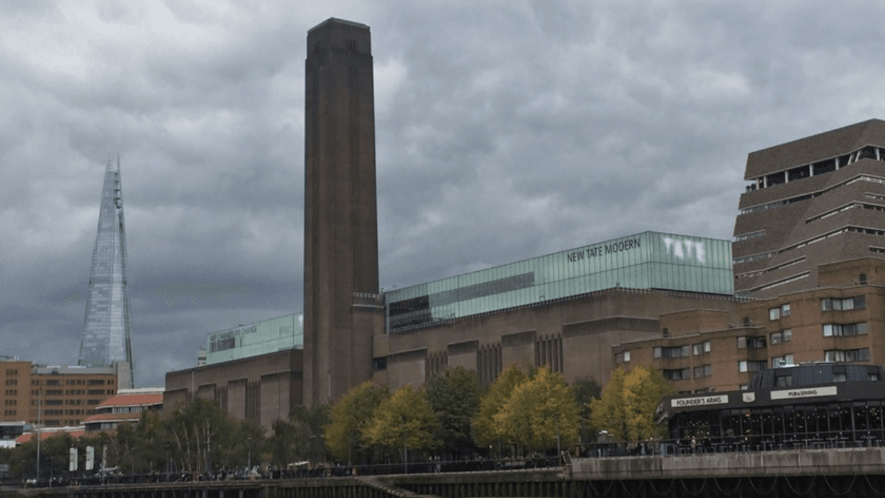 The exterior of Tate Modern, a large former power station with a distinctive brick design and a tall central chimney.